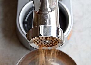 Gemahlene Brotbrösel fallen aus einem Fleischwolf in die Schüssel. Blick direkt von oben.