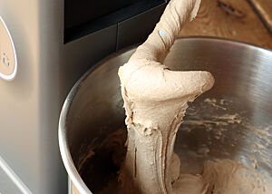 Der helle Teig aus Roggen, Weizen und Dinkel fällt schwerreißend von dem hochgestellten Knethaken.