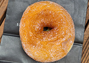 Ein goldbrauner, bezuckerter Bagel liegt auf einer schwarzen Papiertüte.