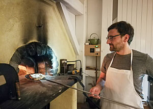 Lutz Geißler holt mit einem Holzschieber ein Fladenbrot aus dem Holzofen.