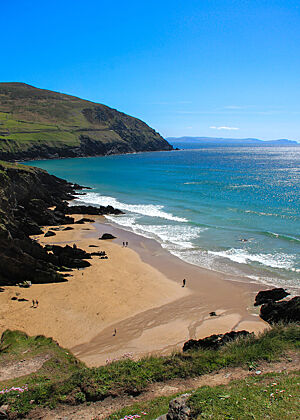 Azurblaues Wasser am Sandstrand vor steil aufragenden Sandsteinen.