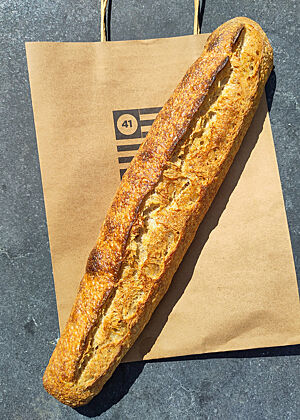 Ein goldbraunes Baguette liegt auf der Papiertüte von Bread 41.