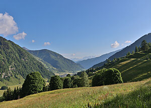Links und rechts des grünen Tals erheben sich waldbewachsene Berge.