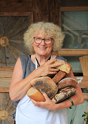 Mit mehreren Broten im Arm steht Roswitha Huber vor der Almhütte.