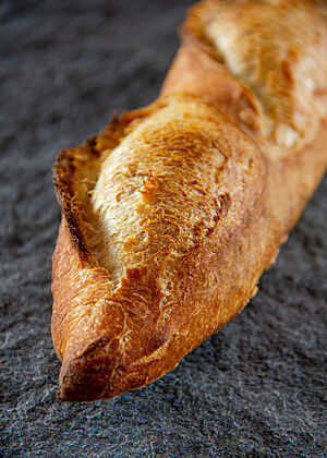 Das goldbraun ausgebackene Baguette ist rustikal aufgerissen und hat spitz zulaufende Enden.