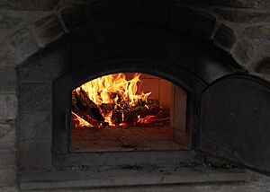 Im offenen Holzofen sind brennende Holzscheite und lodernde Flammen zu sehen.