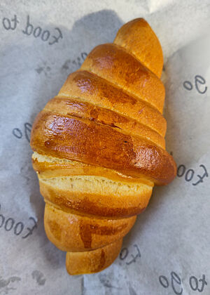 Ein goldbraun gebackenes  „Croissant“ auf Einschlagpapier.