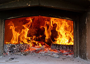Durch die geöffnete Ofentür ist ein loderndes Feuer zu sehen.