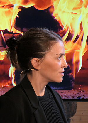 Ava Kundag steht vor einem Bildschirm mit loderndem Feuer.