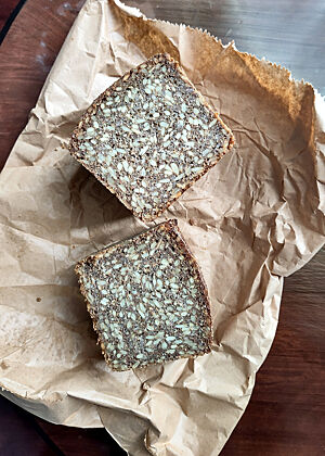 Zwei offenliegende Hälften Schwarzbrot. Deutlich zu erkennen sind die Sonnenblumenkerne, die 50 % der Mehlmenge ausmachen.