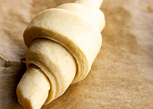Ein Croissant-Teigling, der aus der einmal gewalzten Teigplatte, die anschließend von Hand gerollt wurde, geformt wurde.