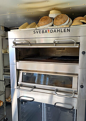 Auf dem Ofen liegen Gärkörbe. Im Hintergrund links steht ein Regal mit Sauerteigen.