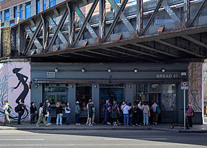 Eine Reihe von Menschen stehen vor der Bäckerei, die sich unter einer Eisenbahnbrücke befindet.