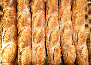 Sechs Baguette liegen auf einem Korbgeflecht.