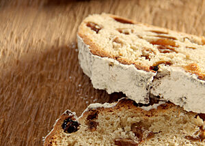 Zwei Scheiben Stollen mit vielen Rosinen in der Krume und Puderzucker auf der Kruste liegen auf einem Holztisch.