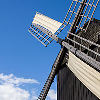 Die Flügel einer alten Mühle ragen in den blauen Himmel.