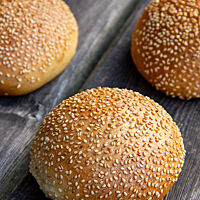 Vier goldbraun ausgebackene, in Sesam gewälzte Briochebrötchen auf einem rustikalen Holztisch. 