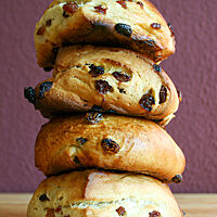 Vier Rosinen-Scones mit Rosinen in der Kruste liegen übereinandergestapelt auf einem Holztisch.