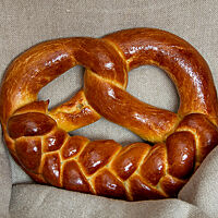Die goldbraun ausgebackene Neujahrsbrezel aus dem zweiten Backversuch hat einen geflochtenen Zopf auf dem Brezelbauch und eine glänzende, ganz wenig gerissene Oberfläche.