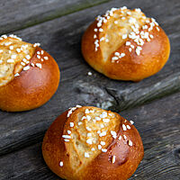 Runde, goldbraun glänzende Brötchen mit rustikalem Aufriss und Hagelzucker auf der Kruste und in der Krume. 