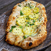 Die Dinnete ähnelt einer Pizza, hat jedoch eine ovale Form und ist statt mit Tomatensauce mit hellem Schmand bestrichen und mit Kartoffelscheiben und Frühlingszwiebelringen belegt.