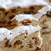 Eine Scheibe des Stollens zeigt die helle, kleinporige Krume mit reichlich Rosinen und die hellbraune, dick mit Puderzucker gestaubte Kruste.