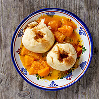 Zwei mit Zimt und Zucker bestreute Hefeklöße liegen auf einem Teller mit Pfirsichkompott.