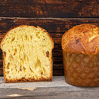 Ein halbierter Panettone mit einer wattig weichen Krume vor einer rustikalen Holzwand.