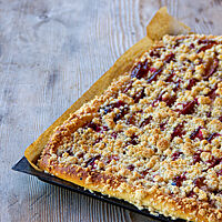 Ein goldbraun ausgebackener Streuselkuchen mit Pflaumen im Blech liegt auf einem rustikalen Holztisch.