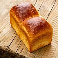 Ein goldbraun ausgebackenes Shokupan mit glänzender Kruste liegt auf einem rustikalen Holztisch.