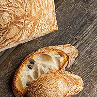 Ein goldbraunes Ciabatta mit grobporiger, heller Krume liegt auf einem Holztisch.