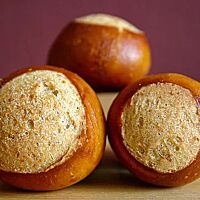 Auf einem hellen Holzuntergrund liegen dunkelbraun ausgebackene Laugenkastanien mit einer glatten, glänzenden Kruste. 