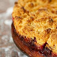 Ein in der Springform gebackener Erdbeerstreuselkuchen liegt auf einer Glasplatte. Am Rand des Kuchens kann man die Schichtung des Kuchens aus Boden, Erdbeeren und Streuseln gut erkennen. 