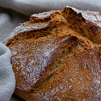 Ein runder Laib mit hellbrauner, bemehlter Kruste und rustikalem Ausbund liegt auf einem hellgrauen Leintuch.