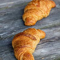 Zwei goldbraun ausgebackene Vollkorncroissants liegen auf einem rustikalen Holztisch.