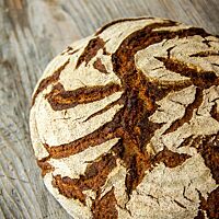 Ein kräftig ausgebackenes, rustikal aufgerissenes Bauernbrot mit bemehlter Kruste liegt auf einem Holztisch.