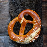 Eine Brezel mit Salz auf der Kruste hängt an einem Nagel an einer rustikalen Holzwand.