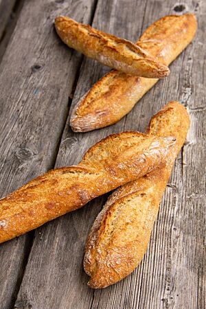 Mehrere Baguettes mit kräftig ausgebackener, knuspriger Kruste liegen auf einem rustikalen Holztisch.