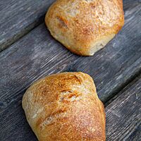 Zwei eckige Brötchen mit glatter, hellbrauner Kruste liegen auf einem dunkelgrauen Holztisch.