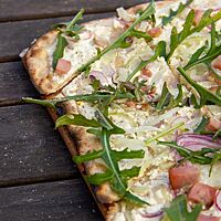 Der Flammkuchen ist großzügig mit Schmand, Zwiebelringen und frischem Rucola belegt.