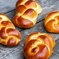 Goldbraun ausgebackene Hefezöpfe mit glänzender Kruste liegen auf einem rustikalen Holztisch.