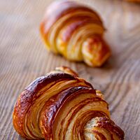 <p>Drei goldbraun ausgebackene Croissants mit glänzender Oberfläche liegen auf einem Holztisch.</p>