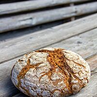 Das kräftig ausgebackene, rustikal aufgerissene Kalchkendlbrot liegt auf einem Holztisch.