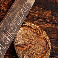 Das kräftig ausgebackene, rustikal aufgerissene Kärntner Bauernbrot mit Brotgewürz auf der Kruste lehnt an einer Holzwand der Kalchkendlalm.