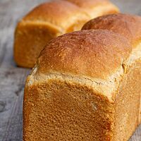 Das ausgebackene Kastenweißbrot mit glatter, unbemehlter Oberfläche liegt auf einem rustikalen Holztisch.