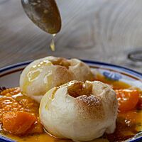 Zwei mit Zimt, Zucker und Butter gefüllte Hefeklöße liegen auf einem Teller mit Marillen-Soße.