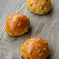 Unter der glatten, stark glänzenden Kruste der Krentenbollen sind die Rosinen mit kleinen Wölbungen sichtbar.