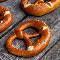 Die mit Brezelsalz bestreuten, glänzenden Laugenbrezeln liegen auf einem rustikalen Holztisch.