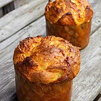 Zwei goldbraun ausgebackene Panettoni mit glänzender Oberfläche stehen auf einem rustikalen Holztisch.