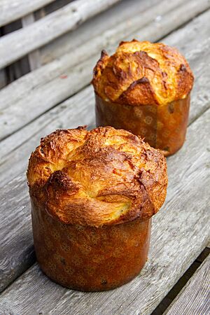 Zwei goldbraun ausgebackene Panettoni mit glänzender Oberfläche stehen auf einem rustikalen Holztisch.